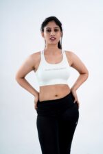 A person in a white sports bra and black leggings stands against a plain background, looking down. The sports bra has the text "Push Your Limits.